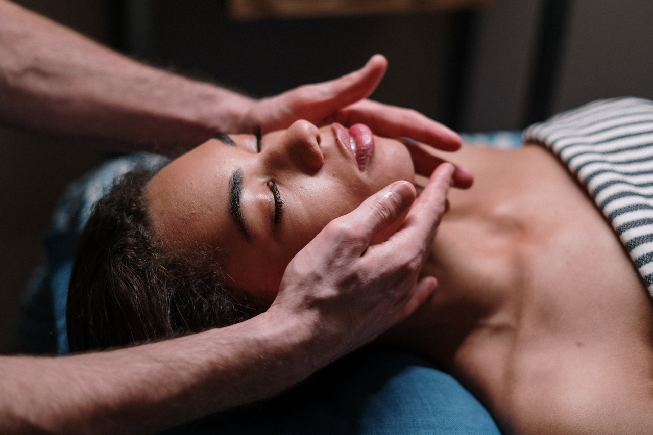 A woman laying on her back on a massage table. The practitioner has their hands on the woman’s face.